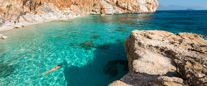 Frau schnorchelt in grichischer Naturkulisse zwischen typischen Felsen im ruhigen türkisblauem Meer vor Korfu.